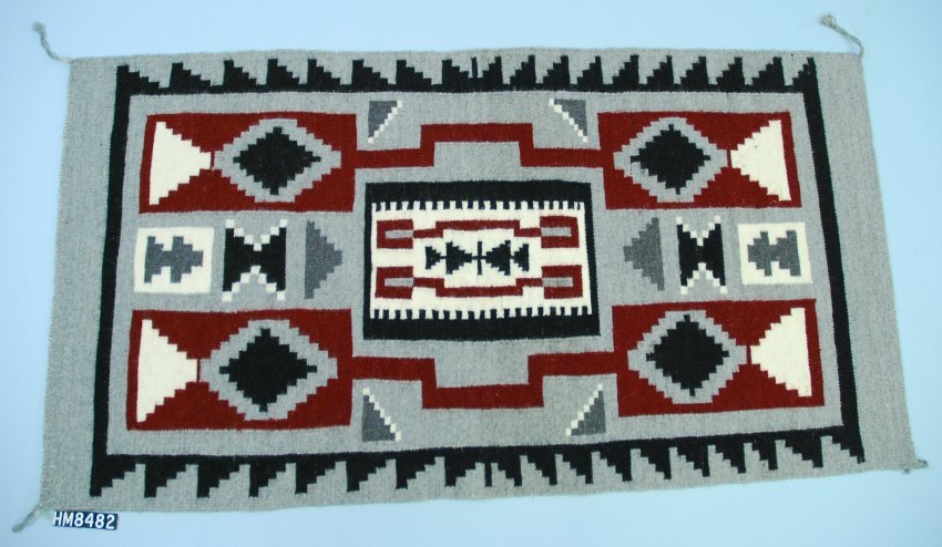 A large woven textile in gray, black, maroon, and cream. Motifs are geometric.