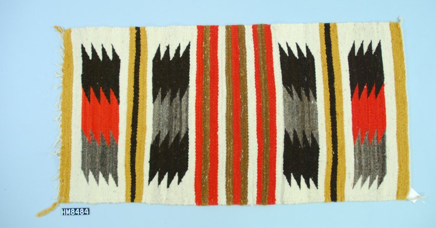 A woven textile in cream, black, gray, red, brown, and gold with motifs organized in stripes.