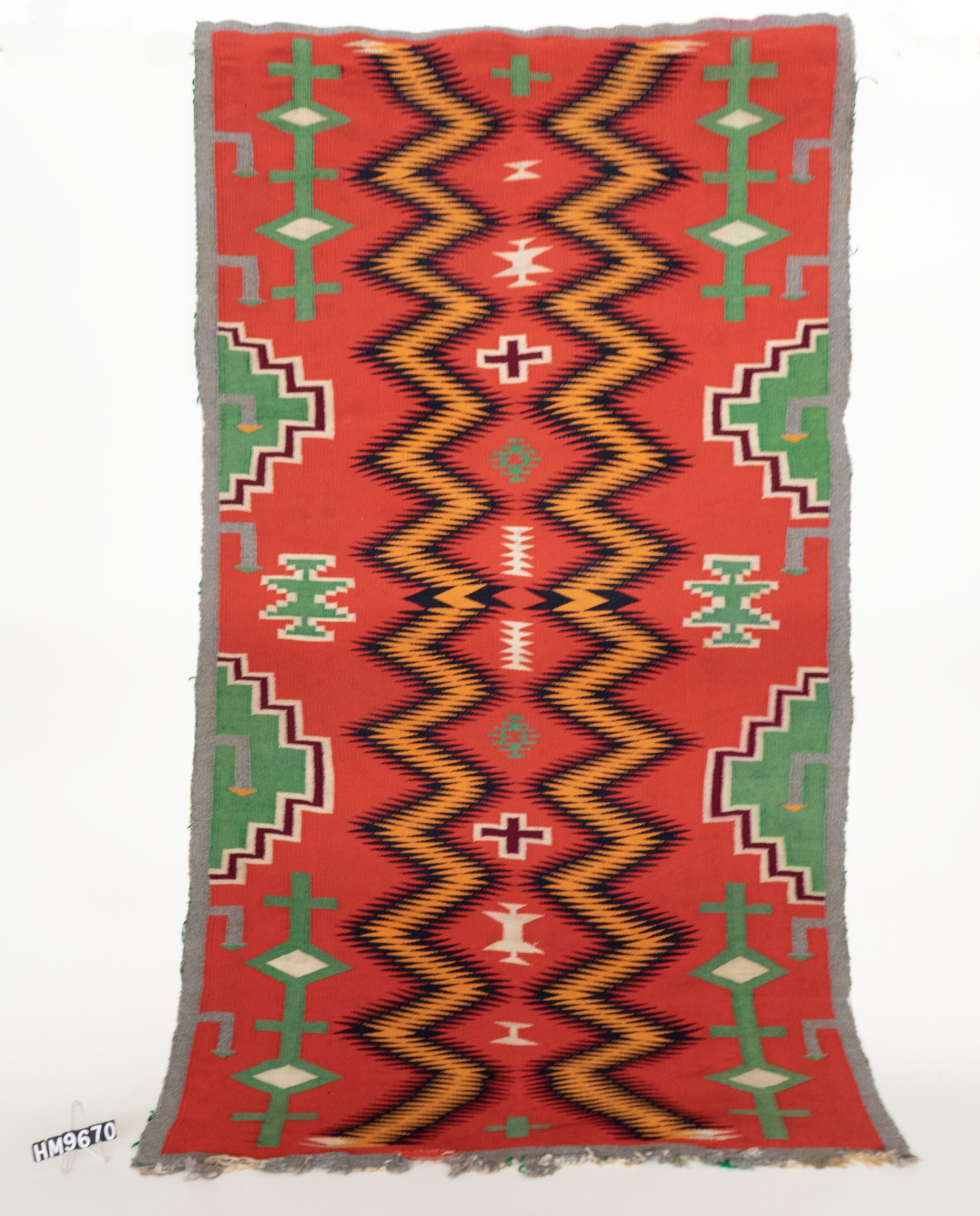 Finely-woven textile in red, green, black, orange, cream, and gray. Patterns with stepped or serrated margins.