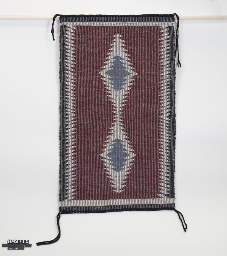 A small woven textile in maroon, black, gray, and blue.