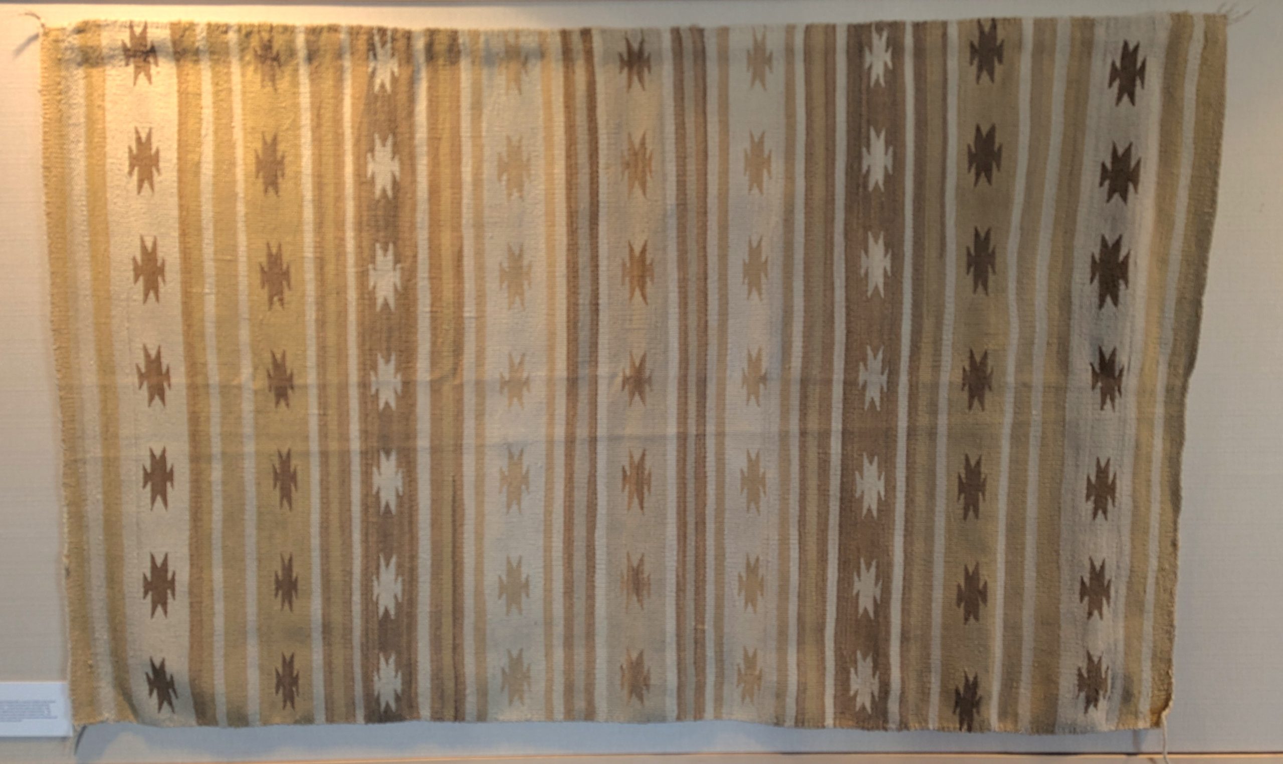 A large woven textile in shades of cream and gold with star and stripe motifs.