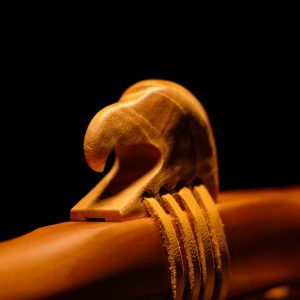 Close up image of an eagle head carved simply from wood and attached with leather to a larger wooden object.
