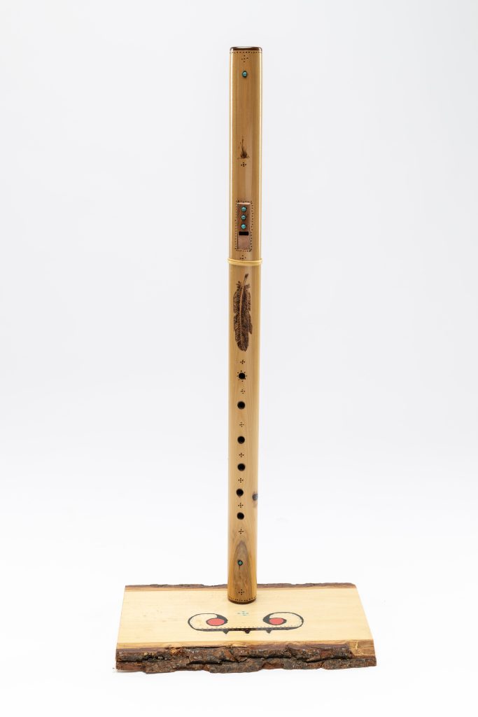 A wooden flute in a stand. The flute is decorated with inlaid turquoise and wood-burned designs.