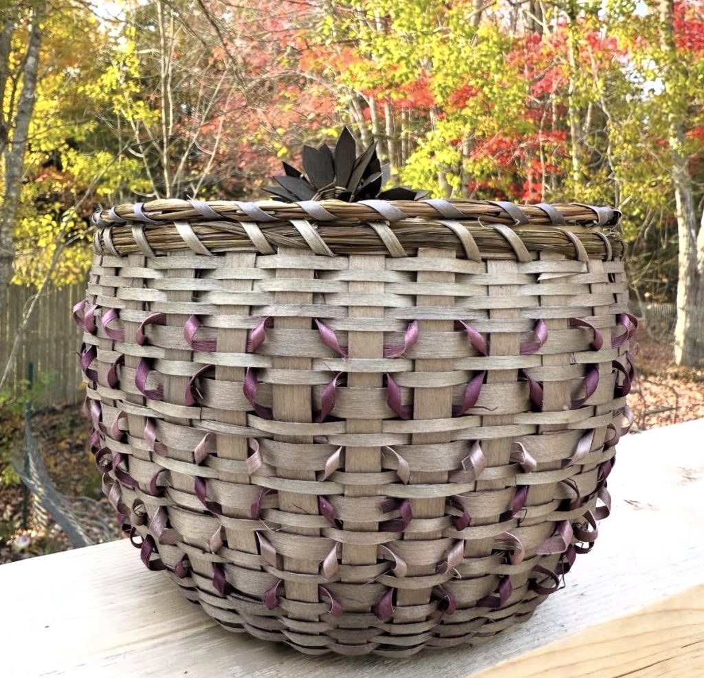 A basket woven in muted colors with delicate curls and a cluster of flowers at the center of the cover.
