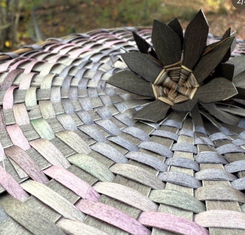 A detail shot of the cover of a basket with muted colors and a cluster of deep green flowers.