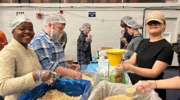 Students standing at assembly table, preparing packaged oatmeal