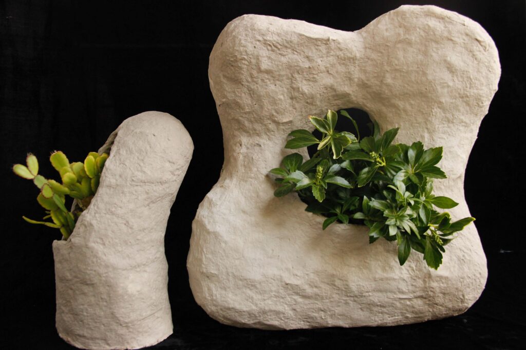 Two sculptural planters made out of paper clay to resemble rocks with plants nested inside them.