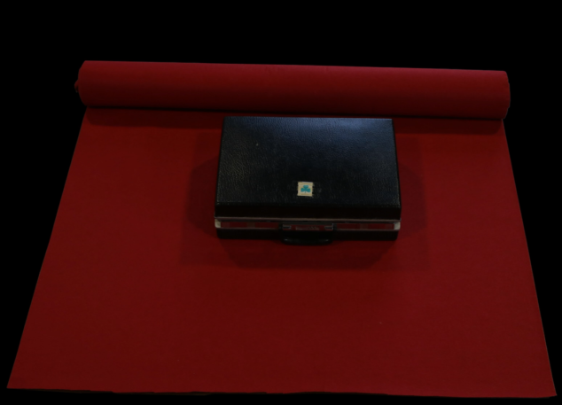 A closed briefcase on a sitting on a rolled out cloth.