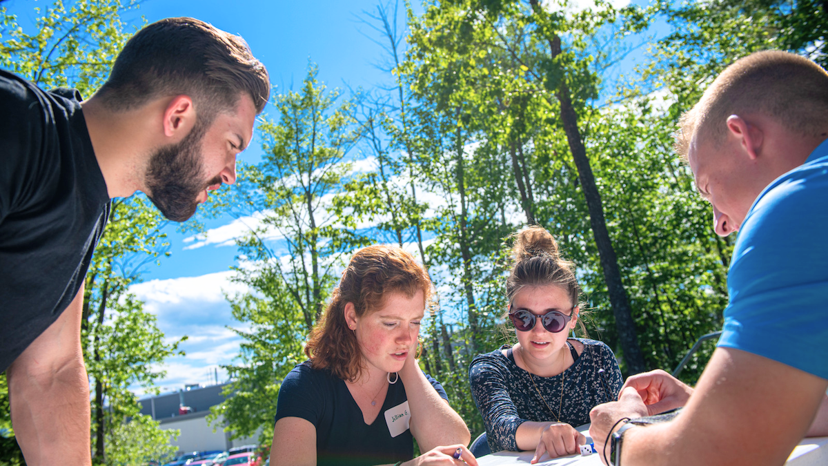 Four students sit around a table outside the Foster Center at UMaine.