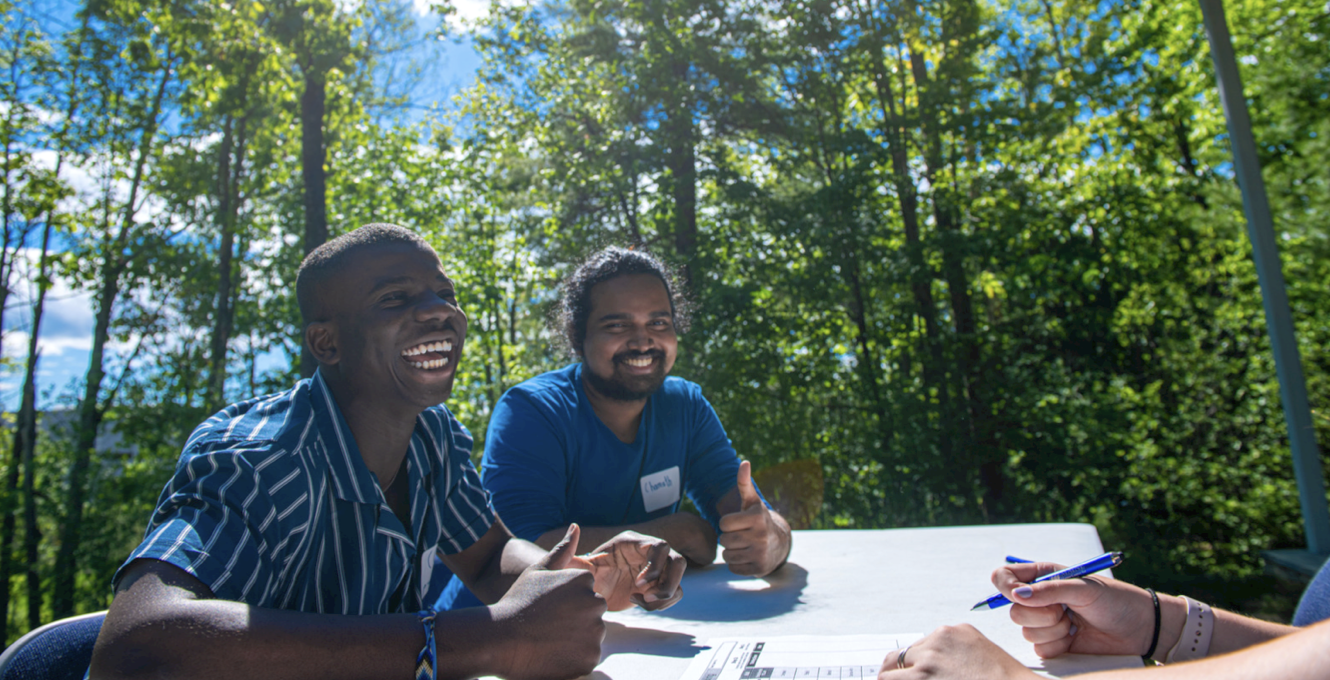Two smiling students seated at a table outside the Foster Center at UMaine.