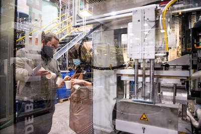 two people are visible through the glass side of a thermoforming machine at UMaine's process development center
