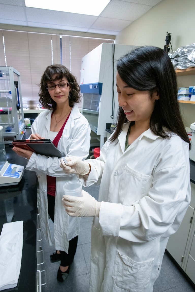 Two female scientists in lab coats stand in a lab