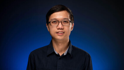 Picture of Khoa standing in front of blue background, smiling