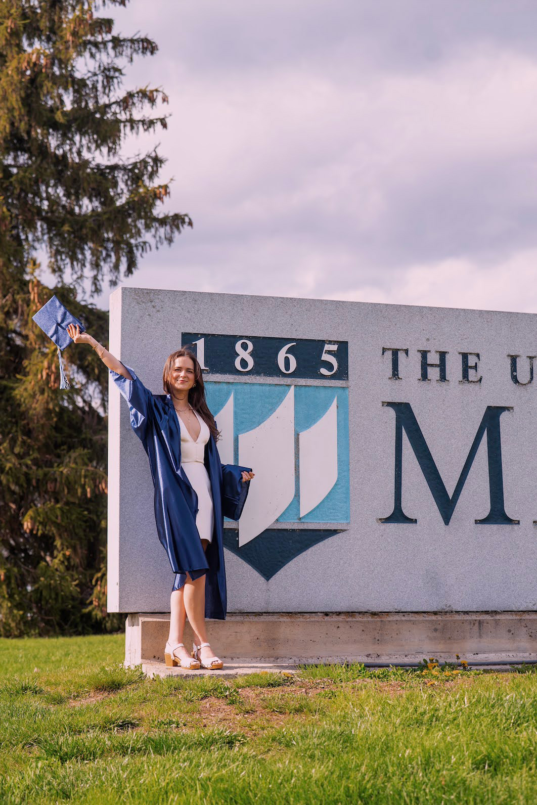 Chemistry graduate in a cap and gown in front of the UMaine sign