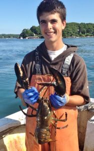 Post Doc Andrew Goode holds a lobster on a deck of a boat.