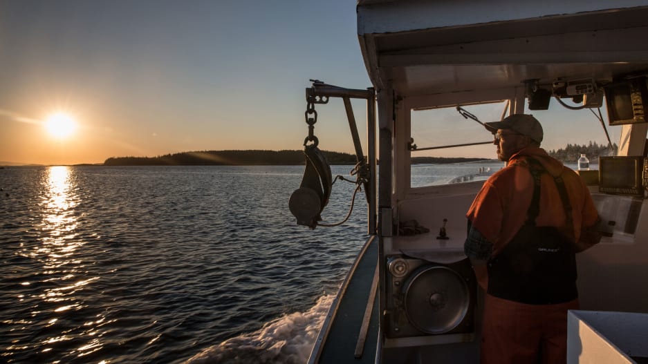 Picture of lobster boat captain at the helm of his boat looking out to sea over his davit.