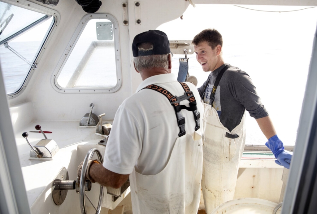 Two men standing the wheelhouse of a lobster boat
