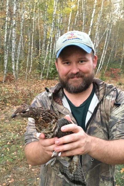 Erik Blomberg holding a grouse in the forest.