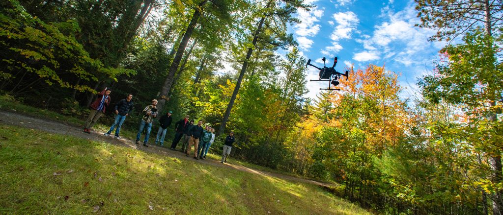 UMaine faculty and students watch a UAV fly to collect LiDAR imagery of the forest.