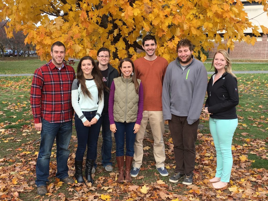 Dr. Maginnis and 6 lab members stand with golden fall foliage behind them.