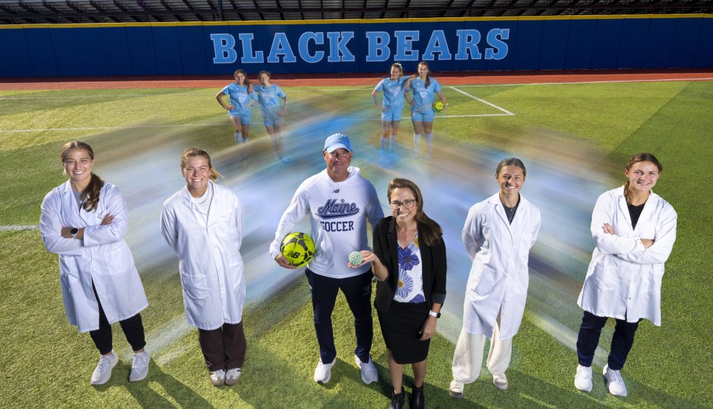 Dr. Maginnis and coach Scott Atherley stand on the soccer field, flanked by two of their shared mentees in lab coats on either side.
