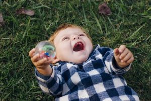 Baby lying on back, laughing, holding ball
