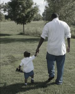 Father and toddler walking in field holding hands
