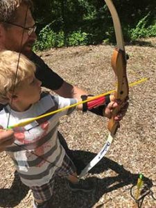 Young boy guided by man to shoot bow and arrow