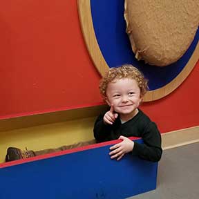 Young boy w curls smiling sitting on floor