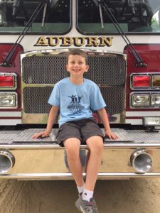 Young boy sitting on firetruck and smiling