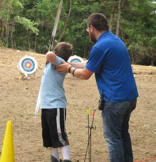 Young boy shooting arrow at target with man guiding him