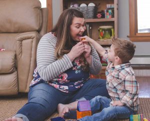 Mother and young child on floor playing with toys, looking at one another