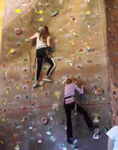 two teen girls climbing an indooor climbing wall