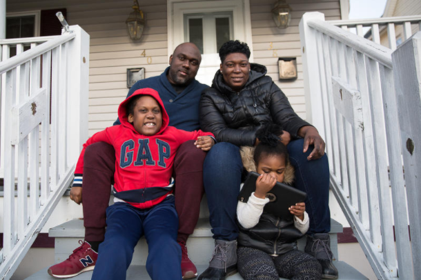 A family with two parents and two children sitting on the steps in front of their home.