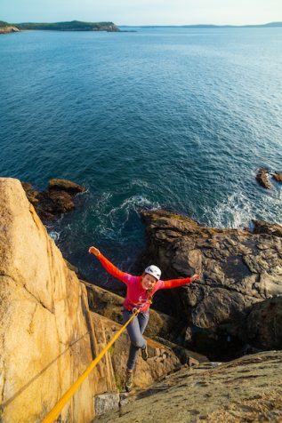 a student hangs on a rope over the ocean with arms out wide smiling