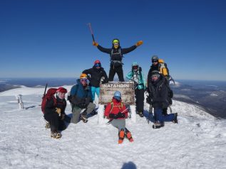 Winter group photo at the katahdin summit sign on a clear blue day.