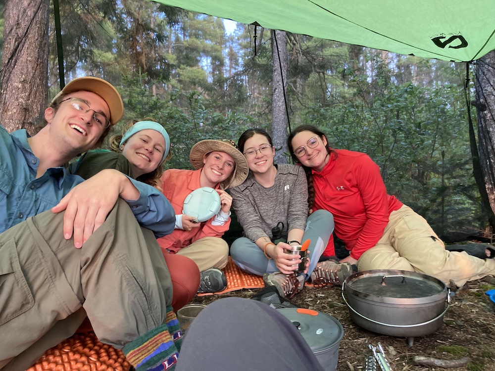 5 individuals sit around a camp kitchen smiling