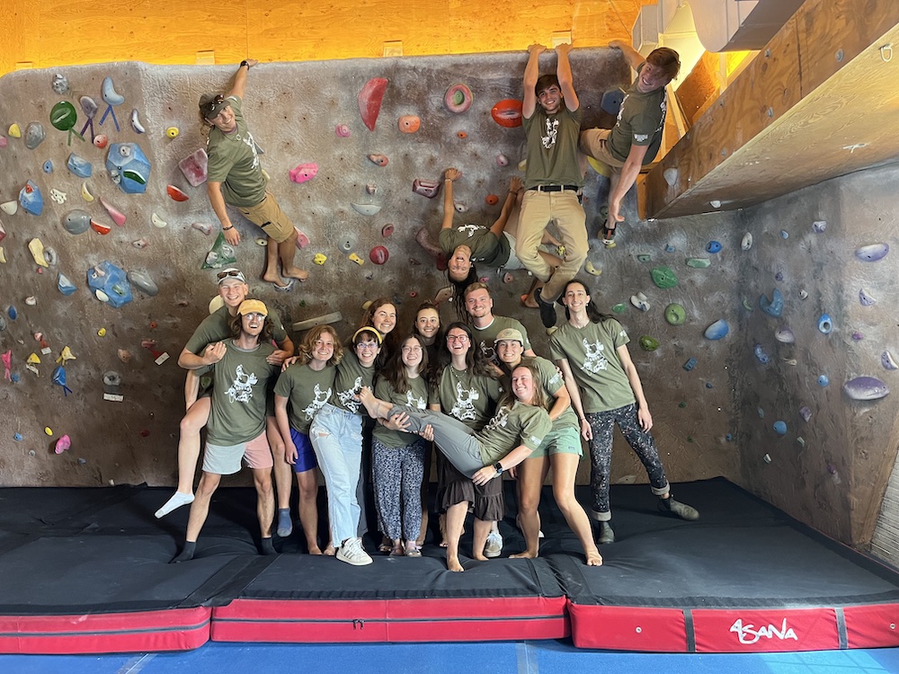 Individuals grouped together in green t shirts smiling in front of the climbing wall