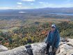 Person wearing blue jacket with hood up has climbing rope draped over her standing in front of fall colored trees