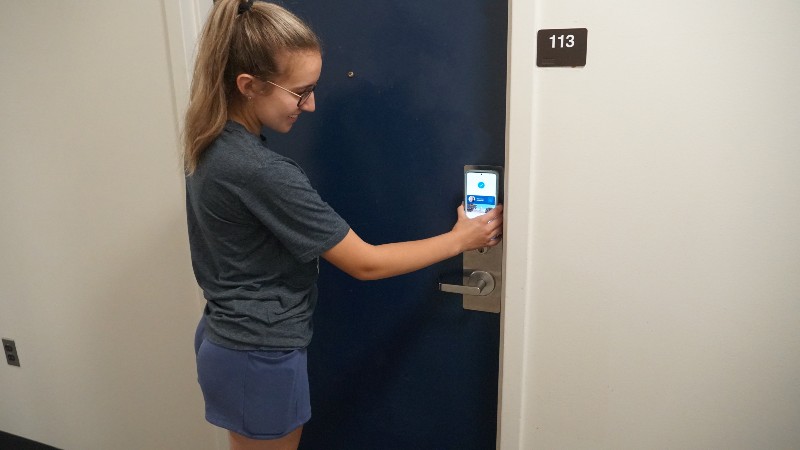 Female student using Mobile MaineCard on room door