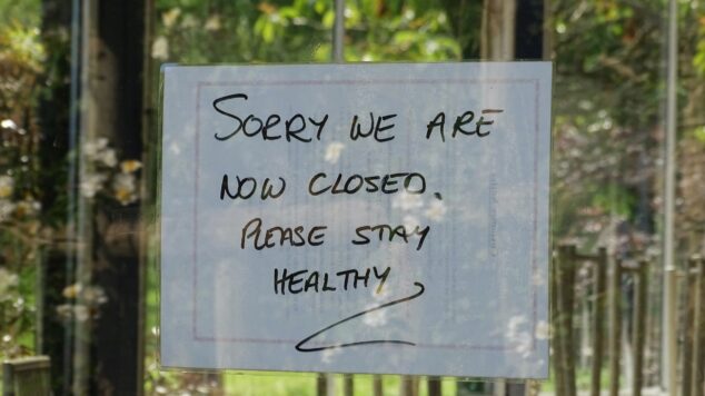 Hand written sign with "Sorry we are closed, please stay healthy" and green foliage reflected in glass window