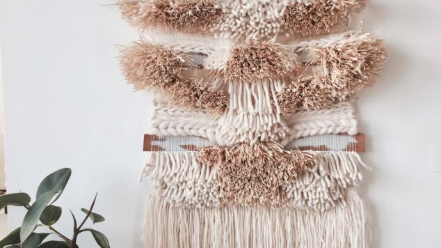 image of woven tapestry hanging on white wall behind a plant
