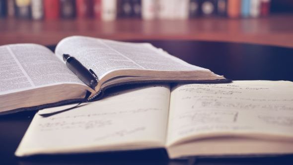Two book lie open on the table. There is a pen in the margin of the left book.