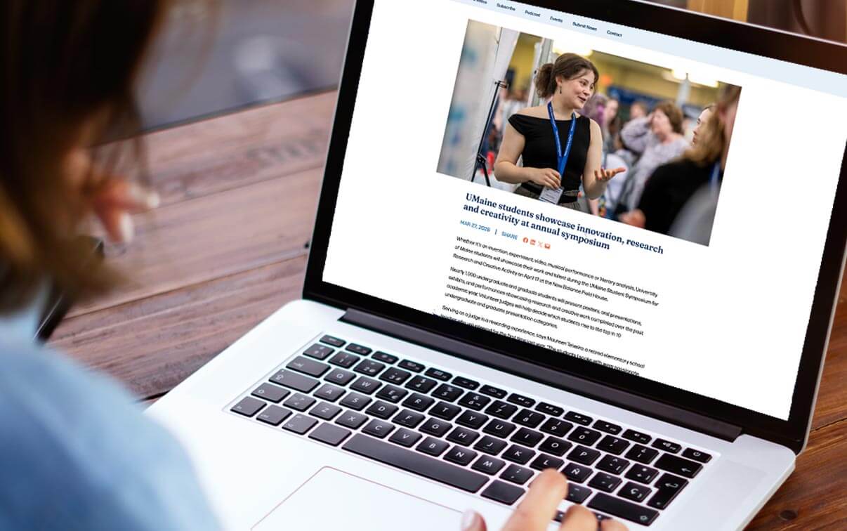 A photo of a person looking at a laptop computer with a UMaine News story on the screen