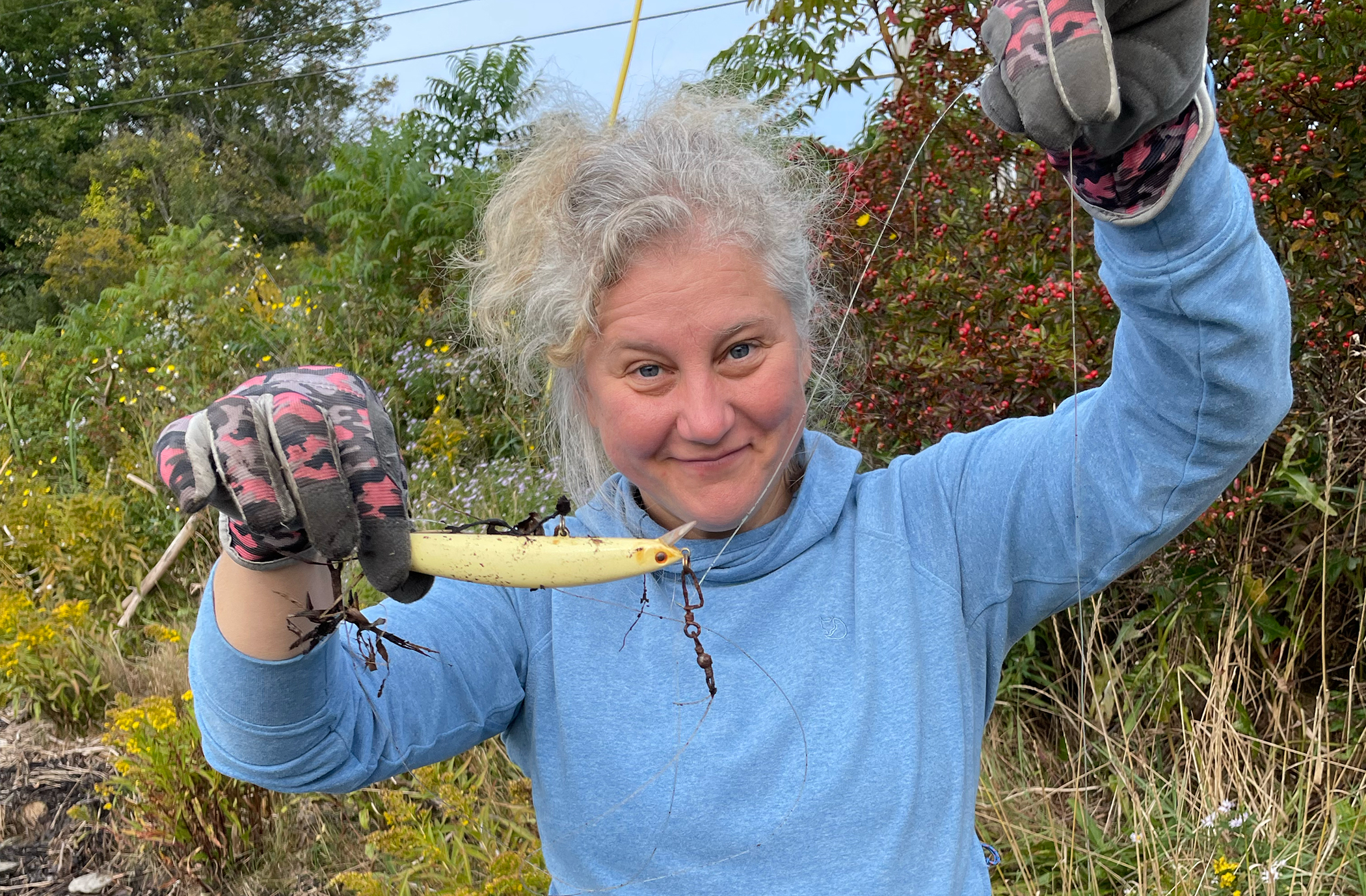 a person in gloves holding up a fishing lure attached to a long line.