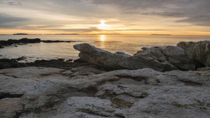 Picture of sunrise over the water on the coast with rocky beach in the foreground.