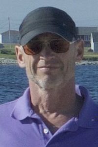 Picture of Andy Thomas standing on rocks on the shore.