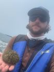 Chandler Sendek on a boat in fog holding a sea urchin
