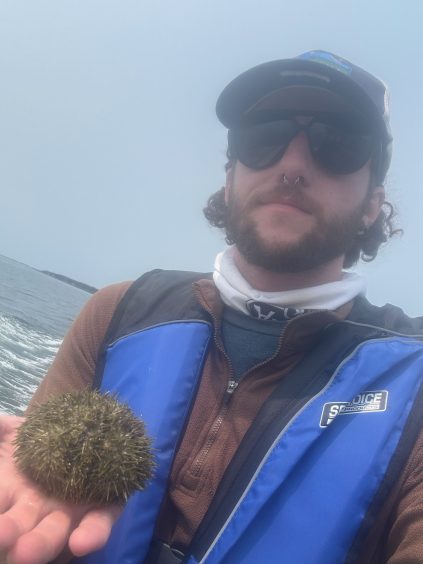 Chandler Sendek on a boat in fog holding a sea urchin