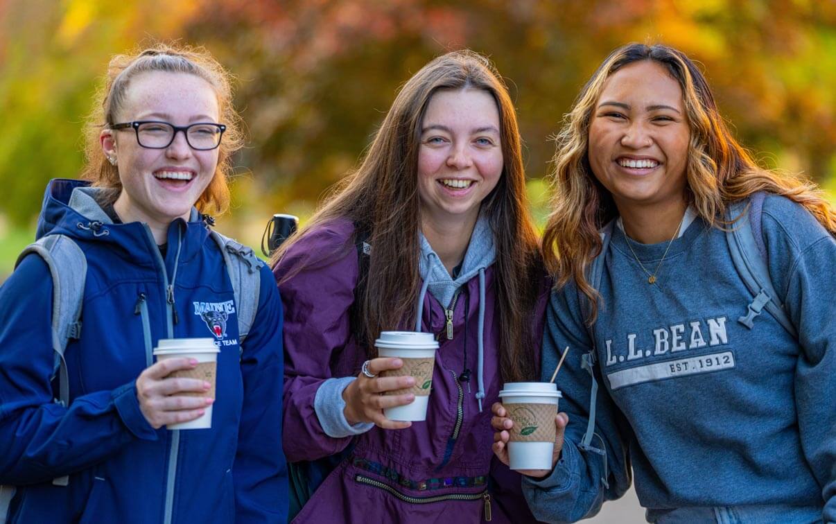 A photo of three students holding coffee cups on a fall day